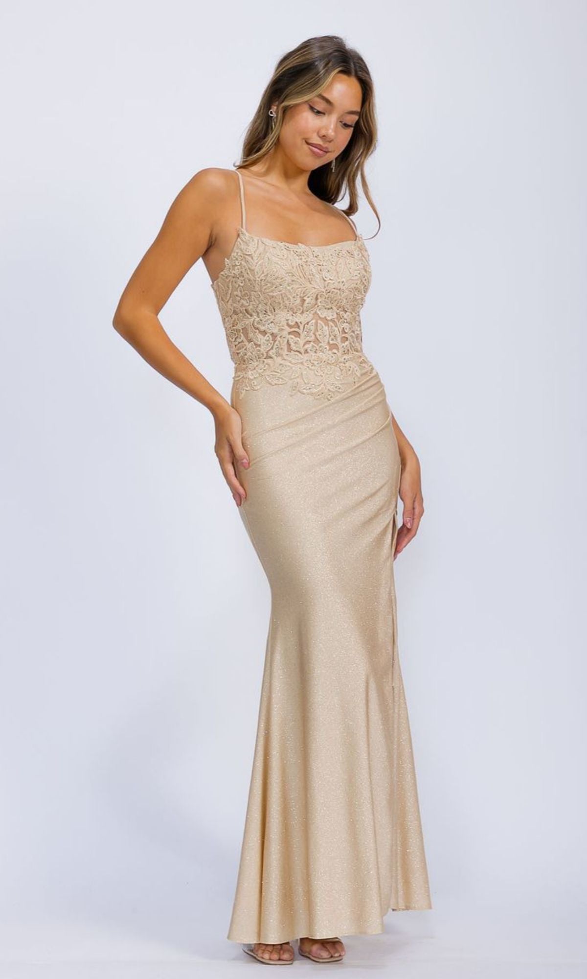 A woman wears the Lace-Corset Long Jersey Prom Dress: Eureka EK129, a light gold, floor-length gown with spaghetti straps and a corset-style bodice, standing against a plain white background.